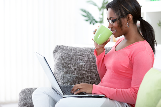 Woman sitting on a sofa drinking coffee working on her laptop