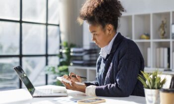 A woman accountant, sitting in her home office, using calculator while working at her computer for blog post work from home math jobs