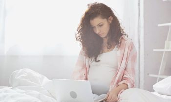 A pregnant woman sitting in bed and using a laptop to work at home.