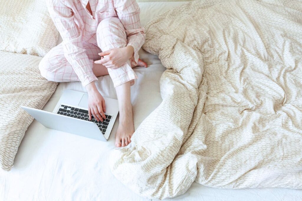 Woman working from home using laptop in bed in pajamas.