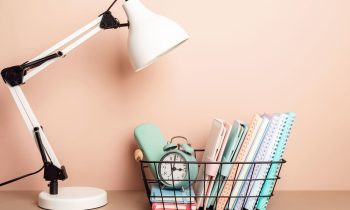 A teacher's home office desk with a lamp and basket of notebooks and school supplies.