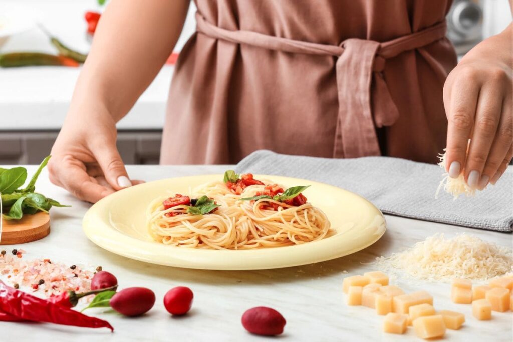 Primer plano de las manos de un chef personal preparando un plato de pasta.