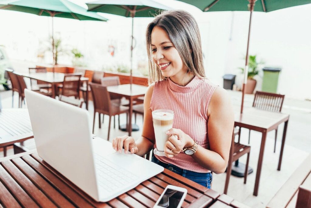 Woman looking for work on laptop while sitting outside at a cafe table.
