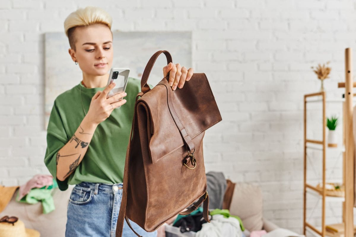 Woman using a phone to take a picture of a used leather bag for selling online.