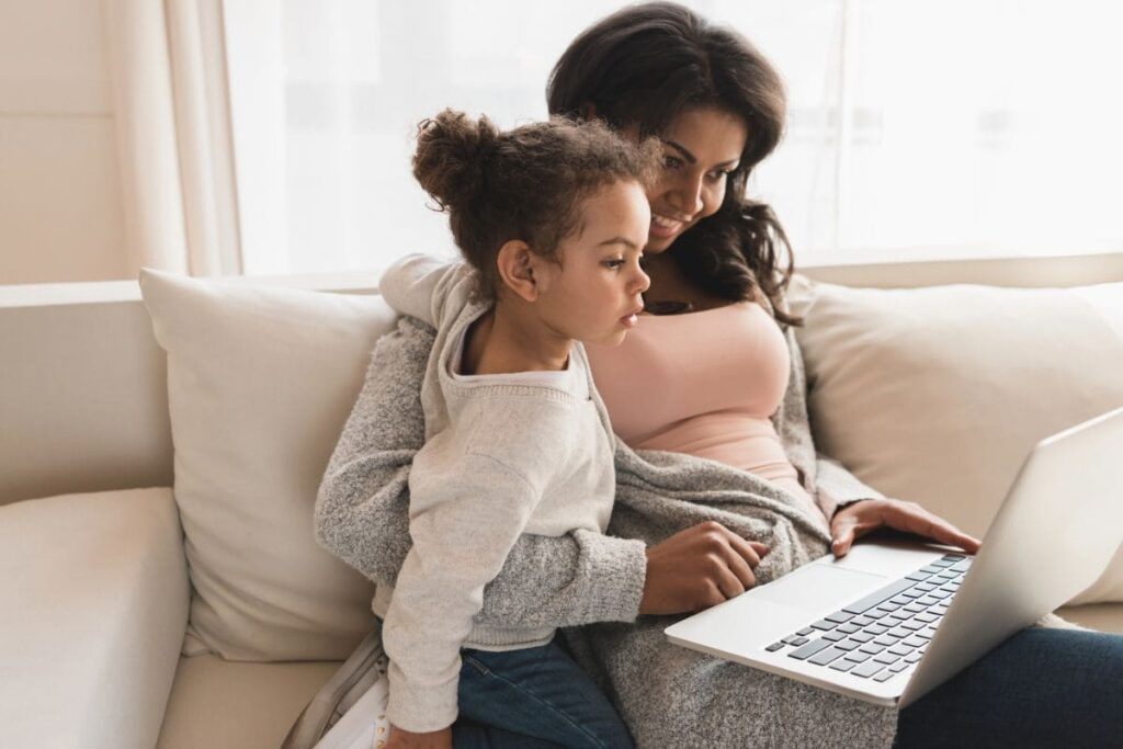 Una madre y una hija pequeña sentadas en el sofá, mirando juntas una computadora portátil.