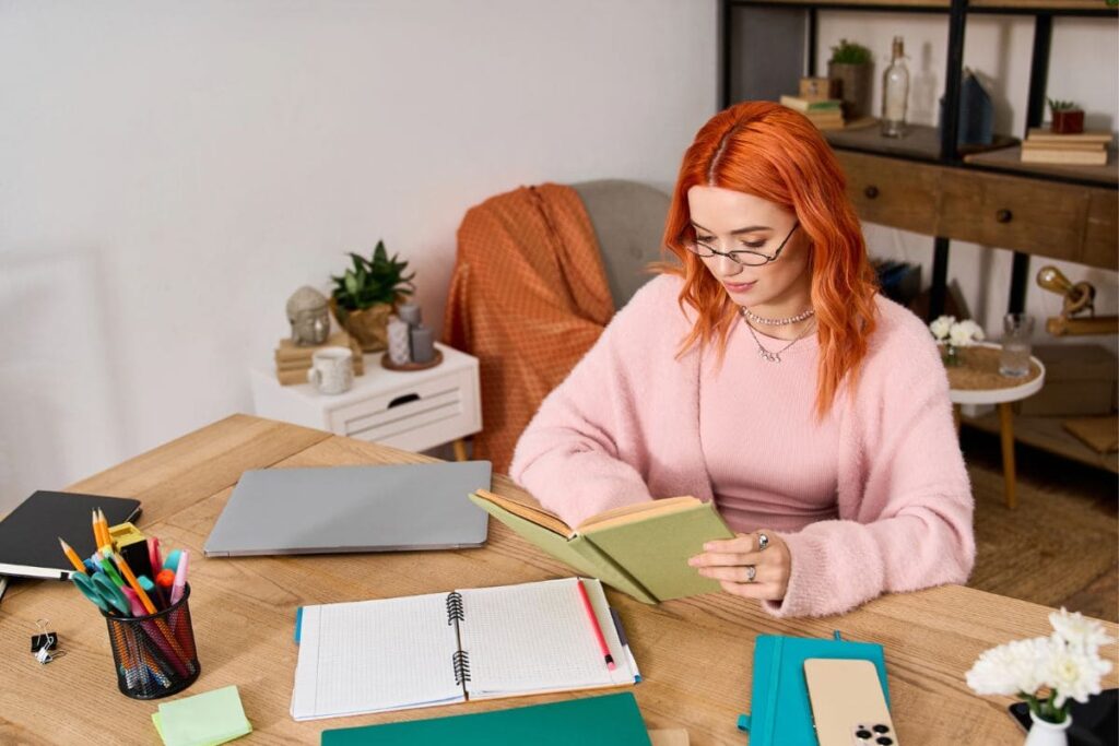 A remote worker sitting at her home office desk, reading a book.