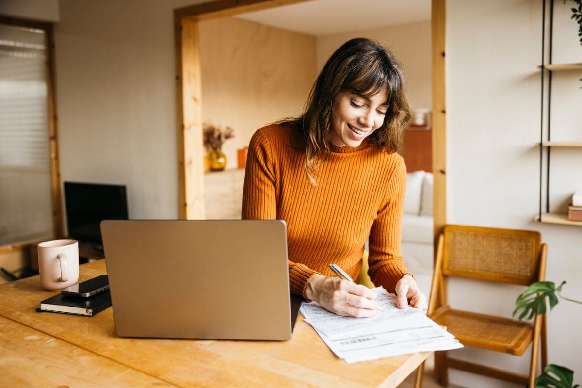 A woman working remotely from her home office desk, using a laptop and writing in a notebook for blog post remote jobs for English majors