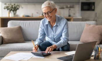 A woman working from home on her couch, using a laptop and calculator for blog post combat ageism.