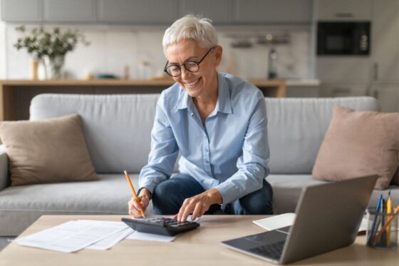 A woman working from home on her couch, using a laptop and calculator for blog post combat ageism.