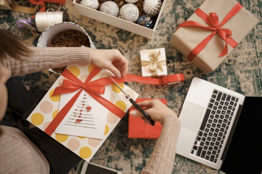 A woman using a laptop while wrapping holiday gifts.