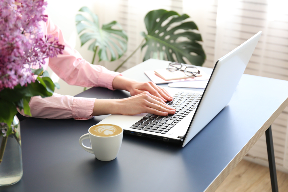 Woman surrounded by plants and flowers working from home on her laptop