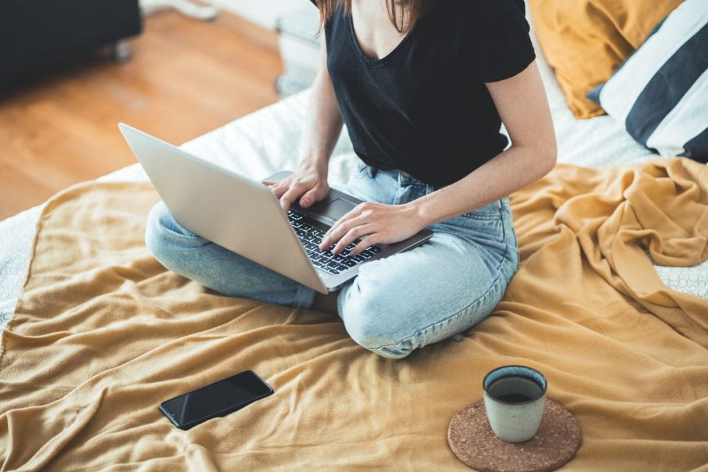 A woman working a remote job from home in bed.