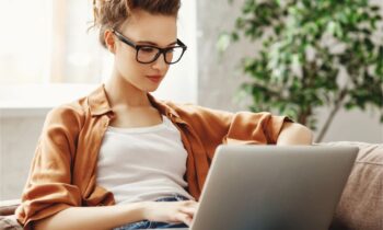 A woman sits on her couch, using her laptop to browse second income opportunities online.