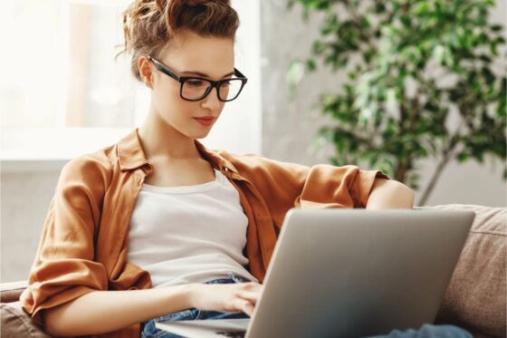 A woman sits on her couch, using her laptop to browse second income opportunities online.