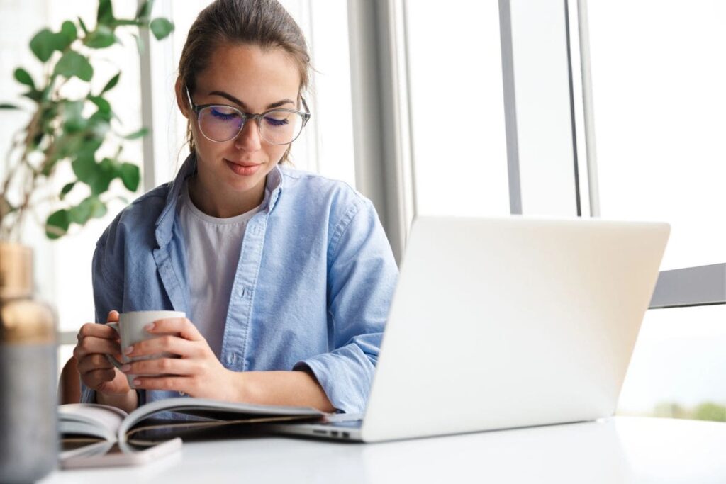 A woman sitting at her home office desk, reading on her laptop.