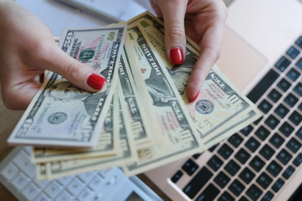 Closeup image of a woman's hands counting cash while using a laptop.