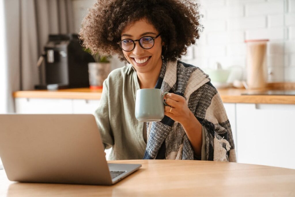 A woman working from home and drinking coffee at her computer.