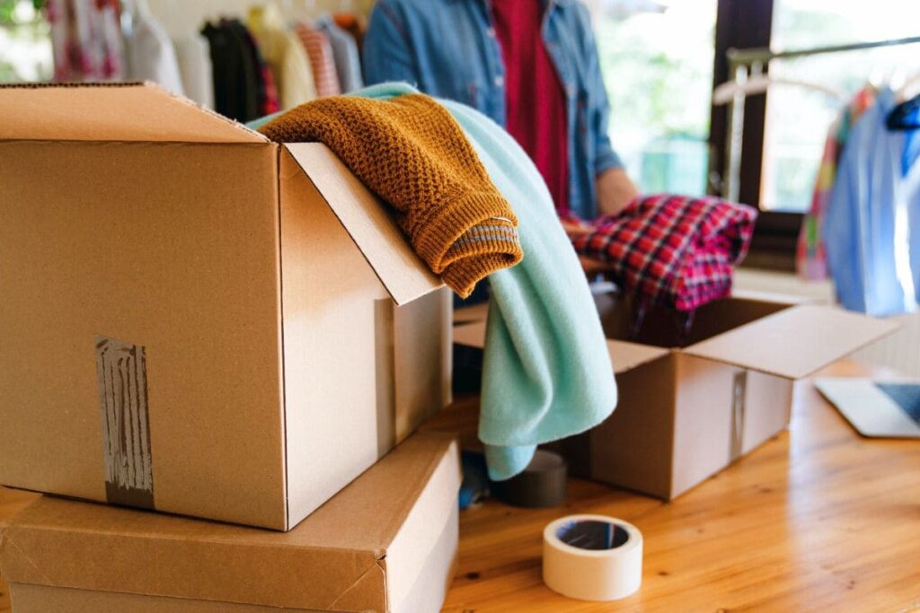 A woman sorting and packing used clothes into boxes to sell online.