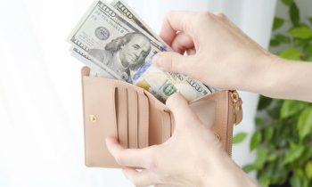 A woman's hands, holding an open wallet with cash for blog post how to make $100 a day