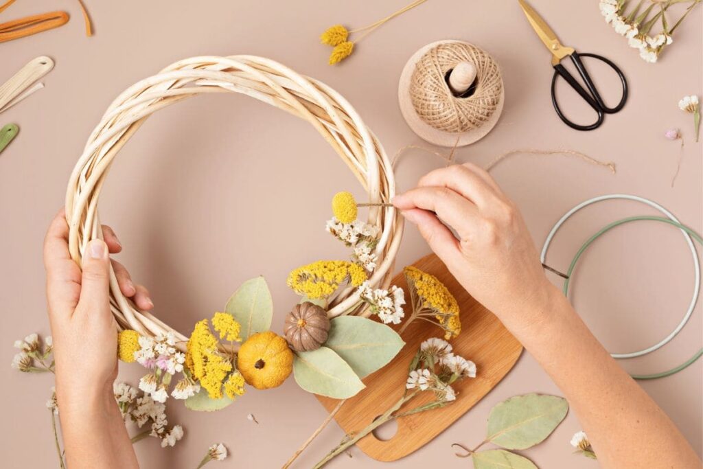 A woman crafting a handmade decorative wreath for the autumn season, with pumpkins and dried flowers.