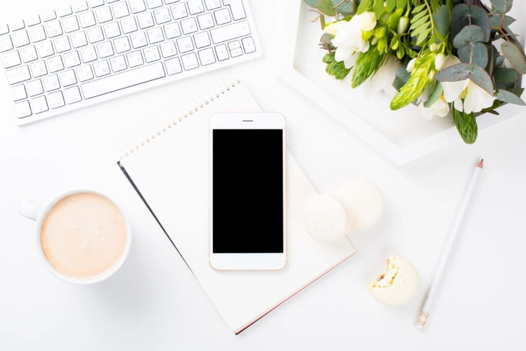 A freelancer's home office desk, with a keyboard, phone, coffee, and notebook.