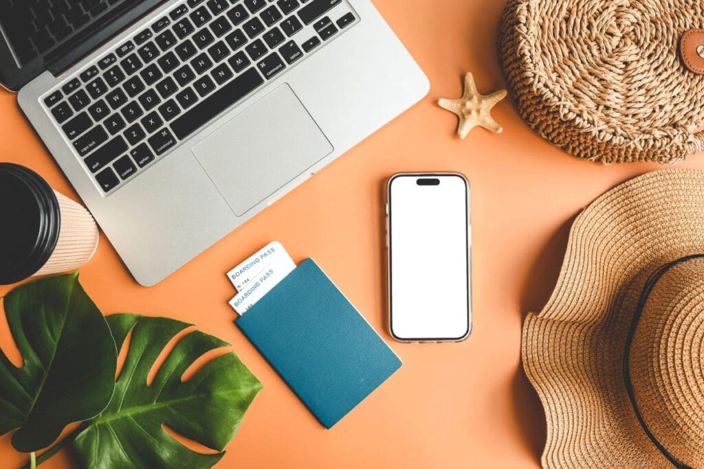 A work from home travel planner's desk, with a laptop, passport, cell phone, and sun hat.