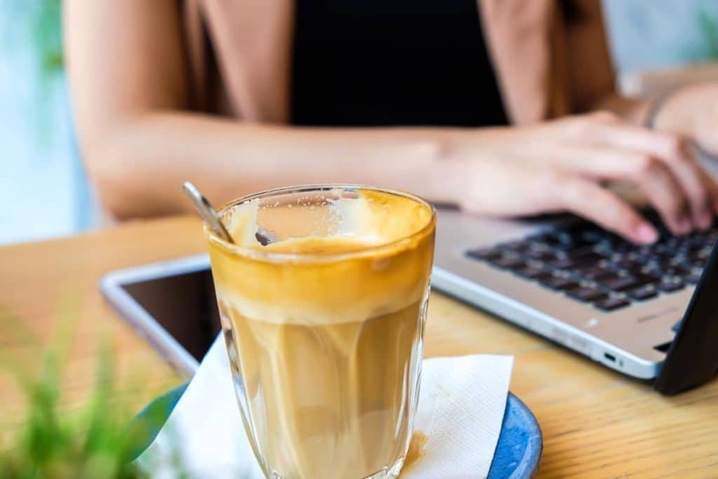 Woman working from home at her desk on a laptop, drinking coffee.