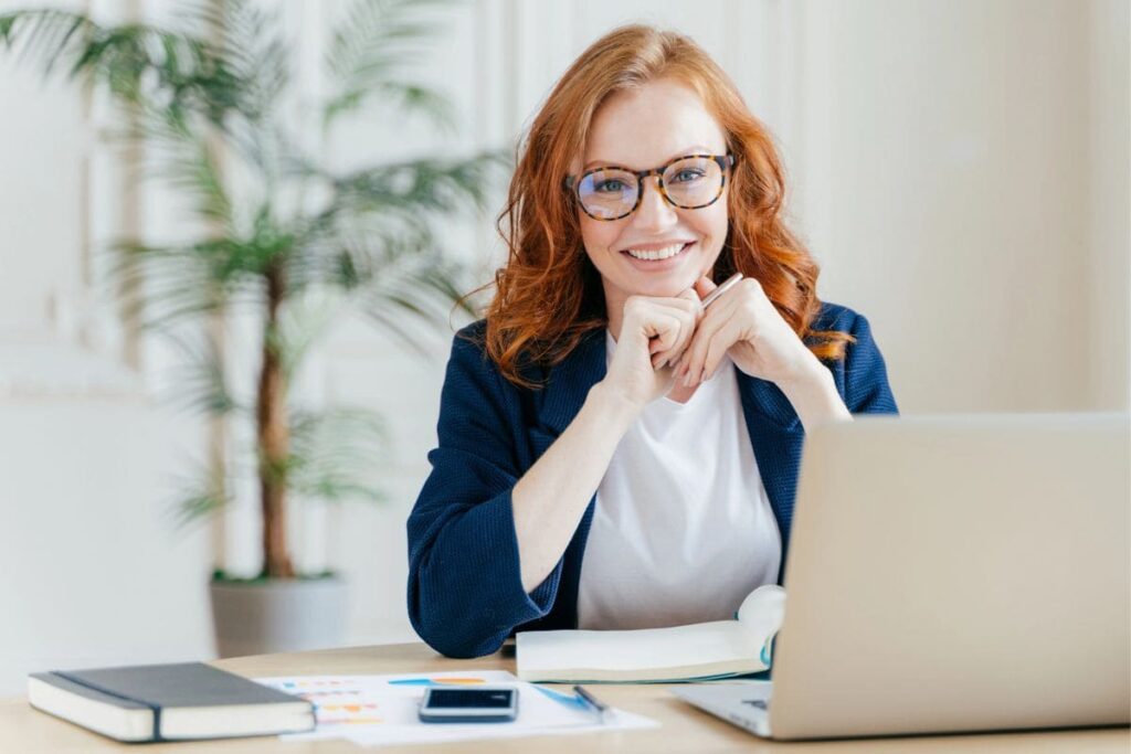 A woman business owner, smiling and sitting at her home office desk.