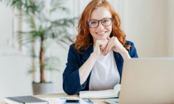 A woman business owner, smiling and sitting at her home office desk for blog post 50 service business ideas.