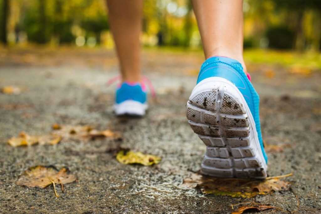 A closeup of a woman's running shoes, running on pavement outdoors.