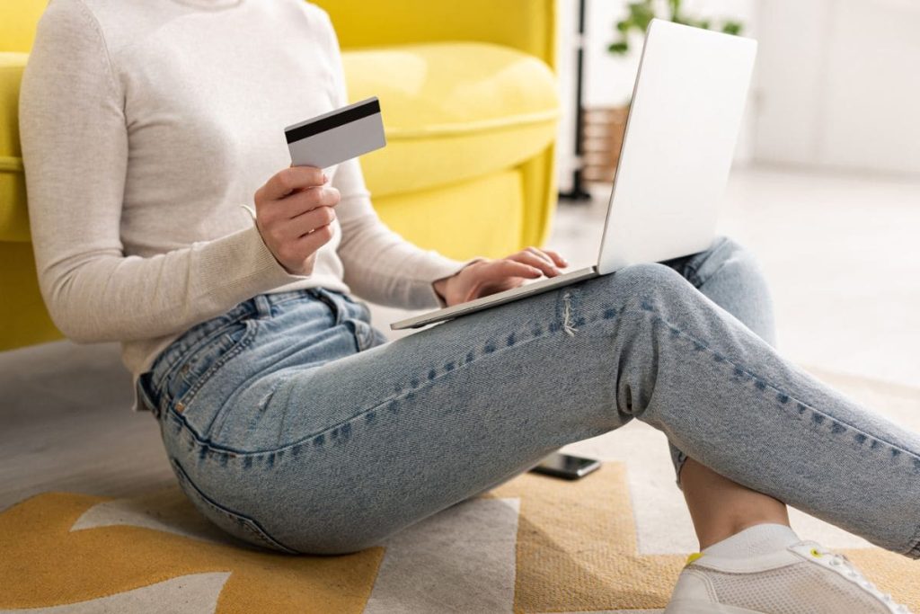 A woman holding a gift card while using a laptop in her living room.