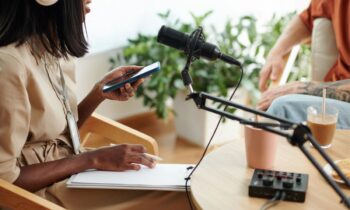 A woman recording a podcast, using a microphone and writing notes on a notepad for blog post how to make money as a content creator