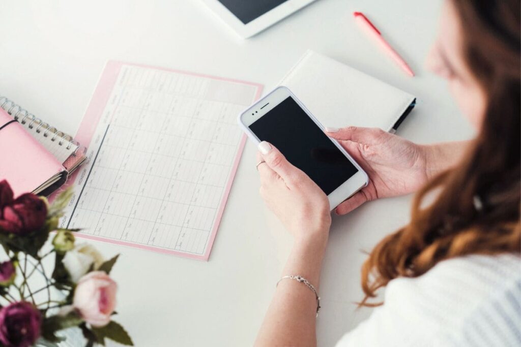 A content creator holding a phone and writing in a calendar.