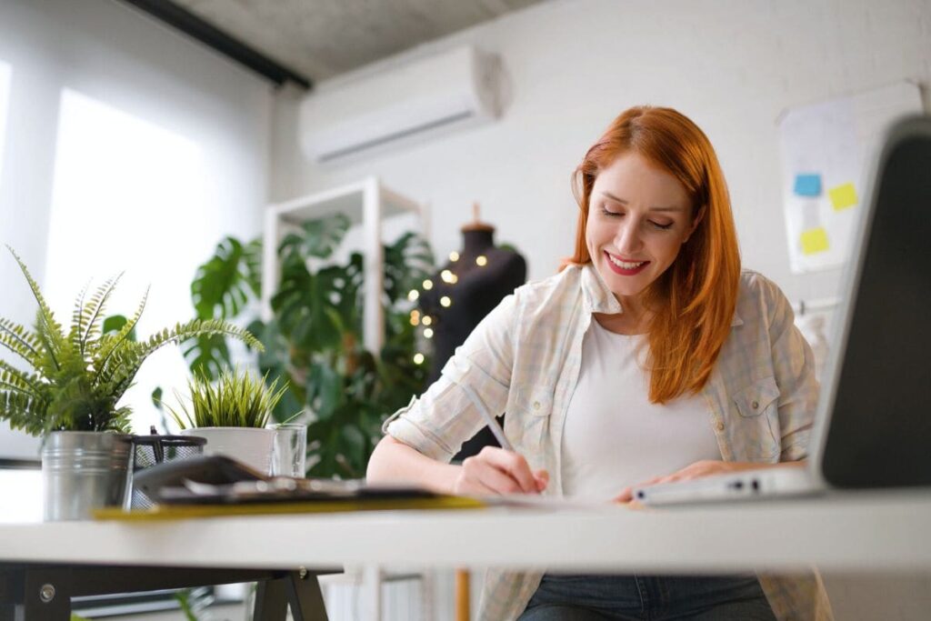 A woman sitting at a desk in her home office, using a computer to apply for remote jobs online.
