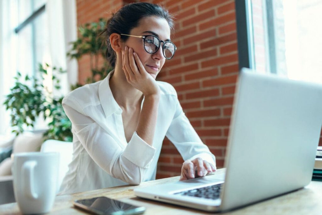 A woman sitting at a desk in her home office, using a computer to apply for remote jobs online.