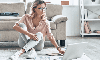 Young woman dressed casually sitting on ground working on laptop