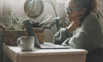 A middle age woman wearing glasses looking at her laptop reading an article on the best jobs for people with chronic illnesses