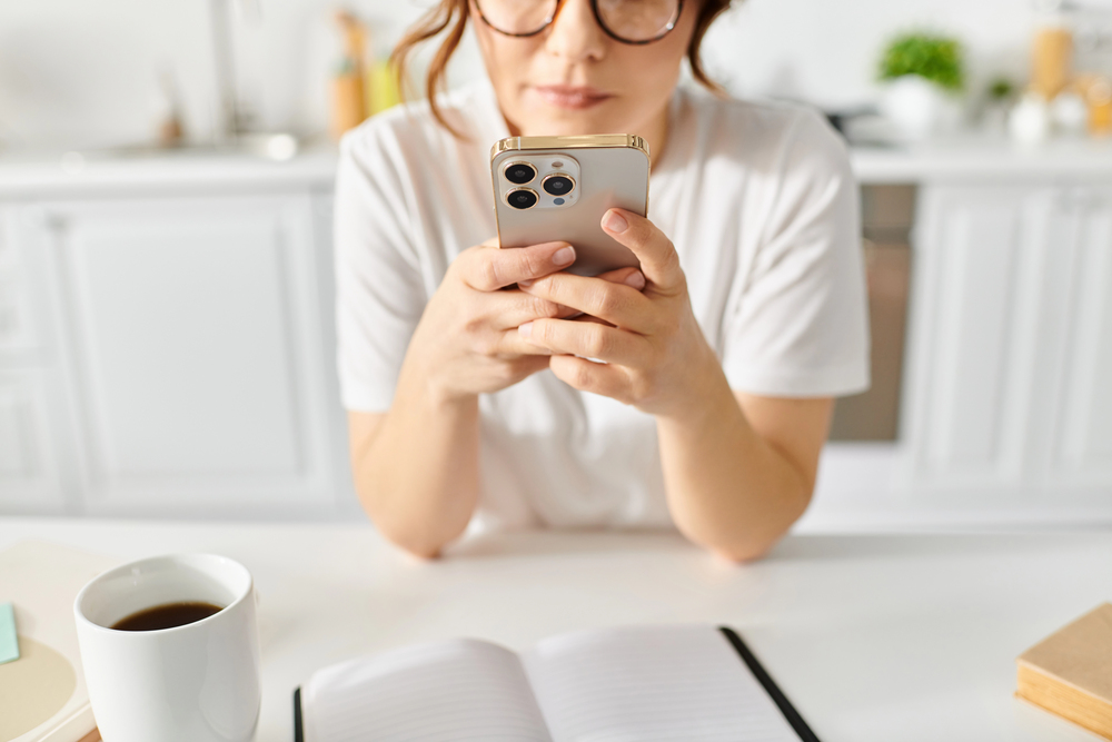 A middle aged female in her kitchen taking surveys using Survey Junkie on her phone