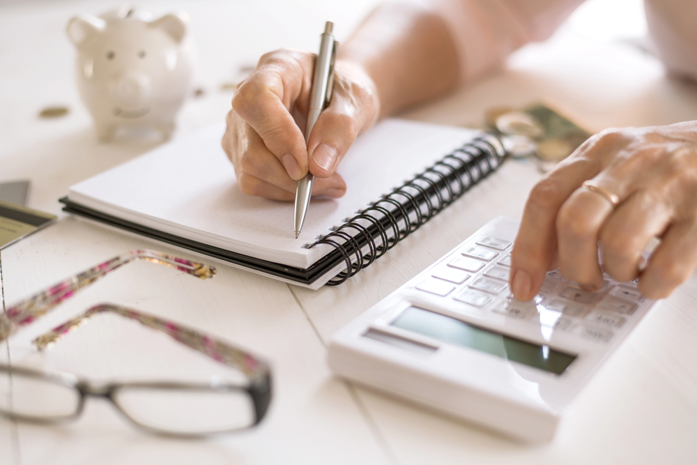 A middle aged woman writing calculations in a notebook trying to earn 100 a day