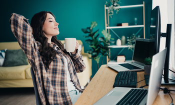 A relaxed young woman leans back in her chair holding a mug researching side business ideas online