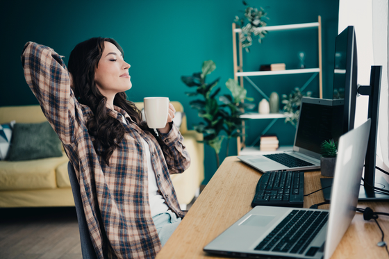 A relaxed young woman leans back in her chair holding a mug researching side business ideas online
