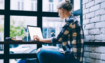 A side view of a young woman reading a User Interviews Review on her laptop in a cafe