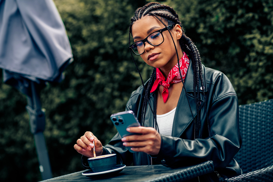 A stylish young woman with braided hair enjoying coffee outdoors and using money-making apps
