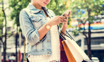 A woman holding shopping bags and her phone completing a mystery shopping gig