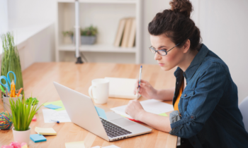 A woman wearing a denim shirt looking at her laptop for a virtual part-time job
