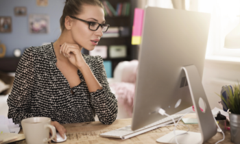 A woman wearing glasses working on her computer searching for a W-2 work from home job
