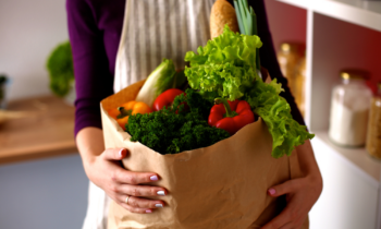 A woman with an apron holding a paper bag of groceries for blog post get paid to shop for others