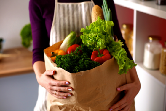 A woman with an apron holding a paper bag of groceries for blog post get paid to shop for others