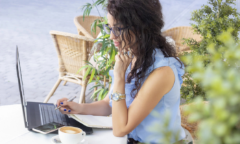 A woman with long black curly hair is wearing glasses working on her laptop, trying to figure out how to make an extra $100 a week