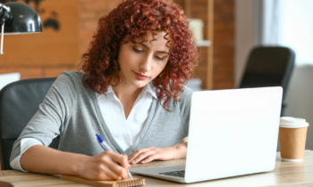 A woman with red curly hair writing in her notebook for blog post resume writers
